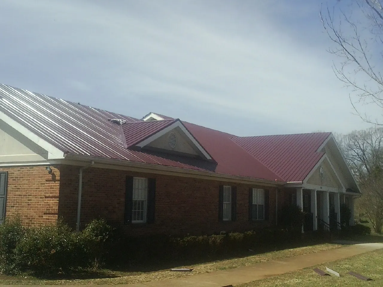 Red metal roof with gabled entries on a long brick building, from a Hail Damage Roof Repair job in Dade City