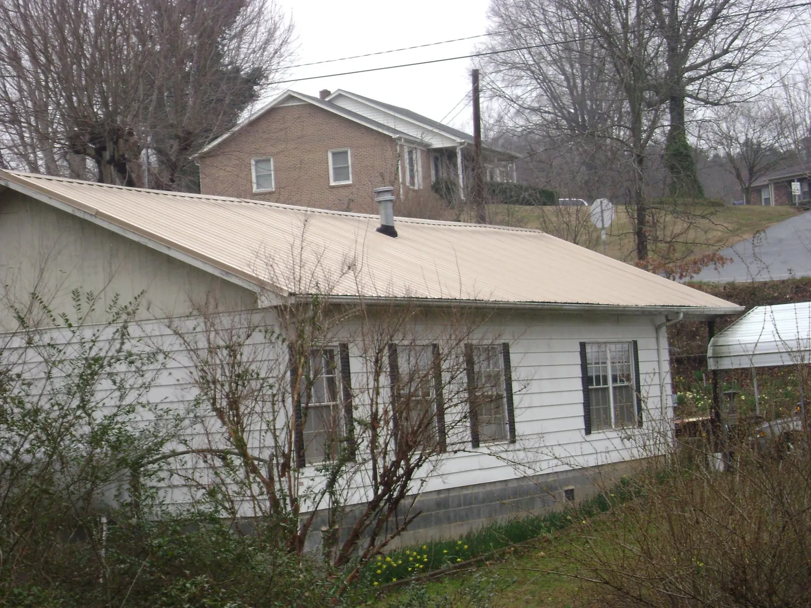 Tan metal roof on a white sided house set into a hillside — Commercial Roofing by Roofing Brothers in Dade City